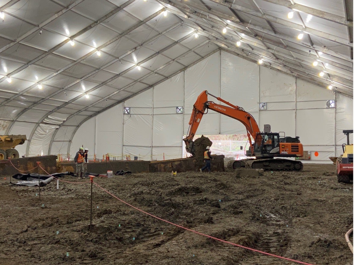 inside of a giant canvas tent with lights on the ceiling and a large construction shovel digging