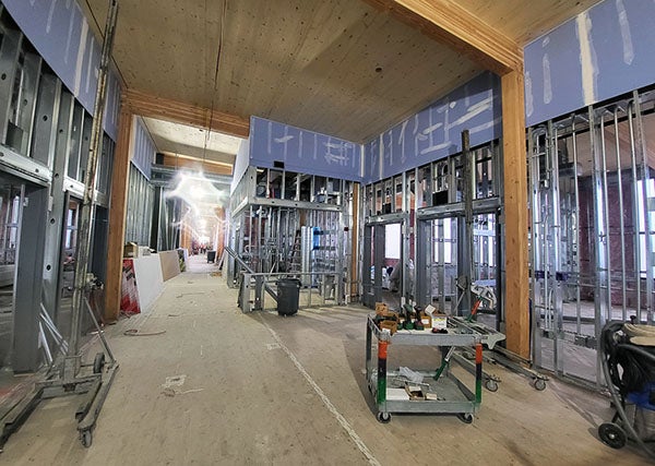 interior of a building under construction with high wood covered ceilings, wood post and beams, and metal wall studs with wallboard on the upper part of the wall