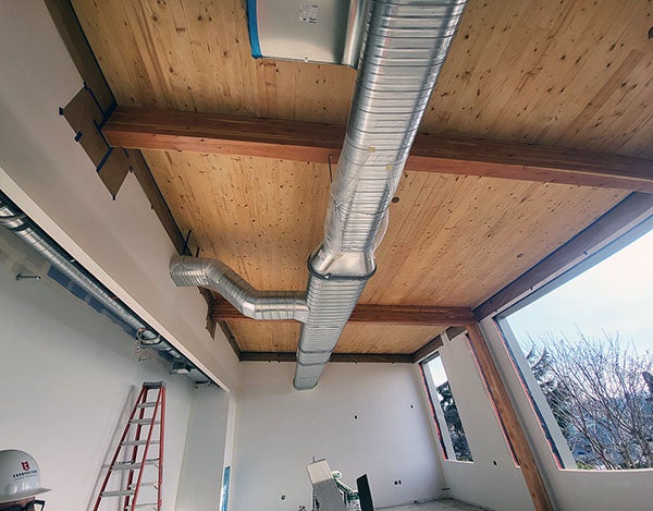 looking up toward a wood ceiling with a metal duct running across it. openings in the wall for windows are empty, wallboard is painted