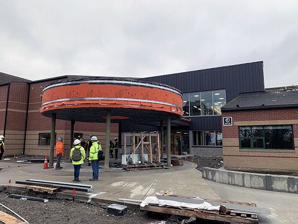 a brick building has a round canopy with orange sheathing. construction workers and materials are in the photo