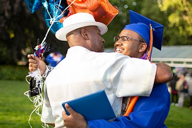 A student in cap and gown hugs an adult during a graduation ceremony 