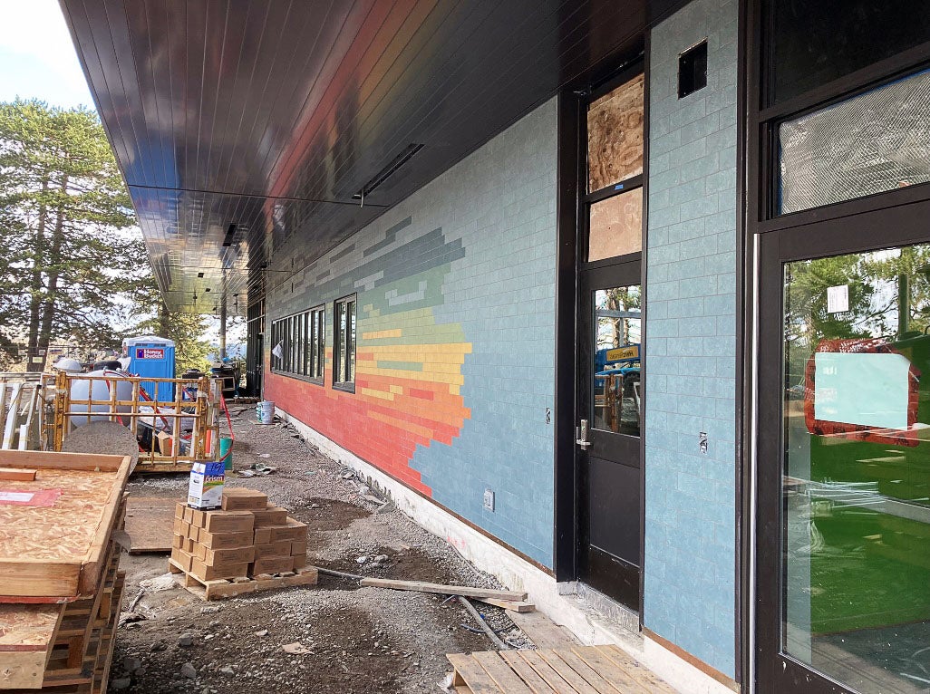 an exterior wall with a door has blue tiles and tiles of other bright colors being installed in stripes