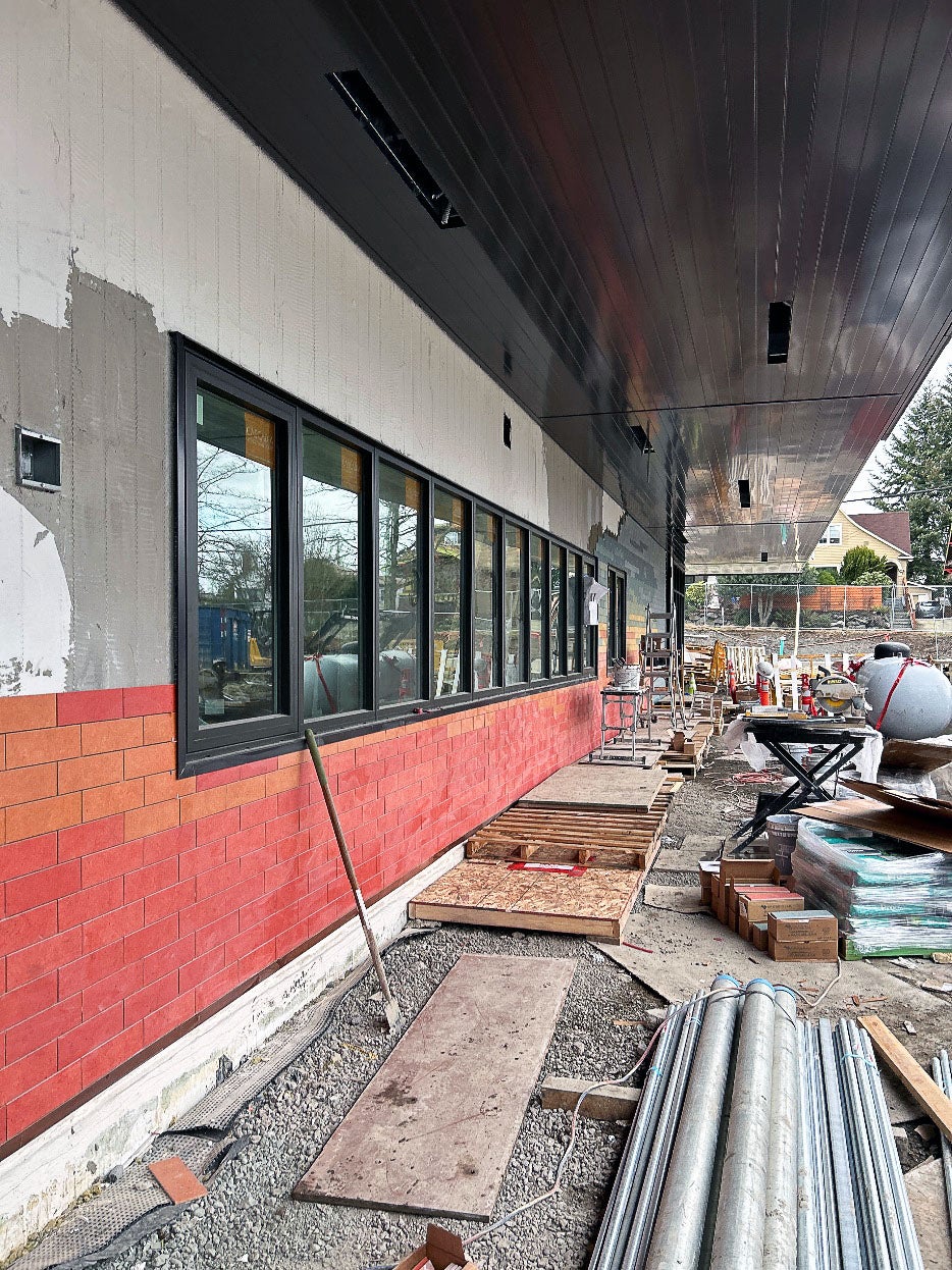 exterior windows under a roof overhang have varying colors of orange tiles being installed in stripes