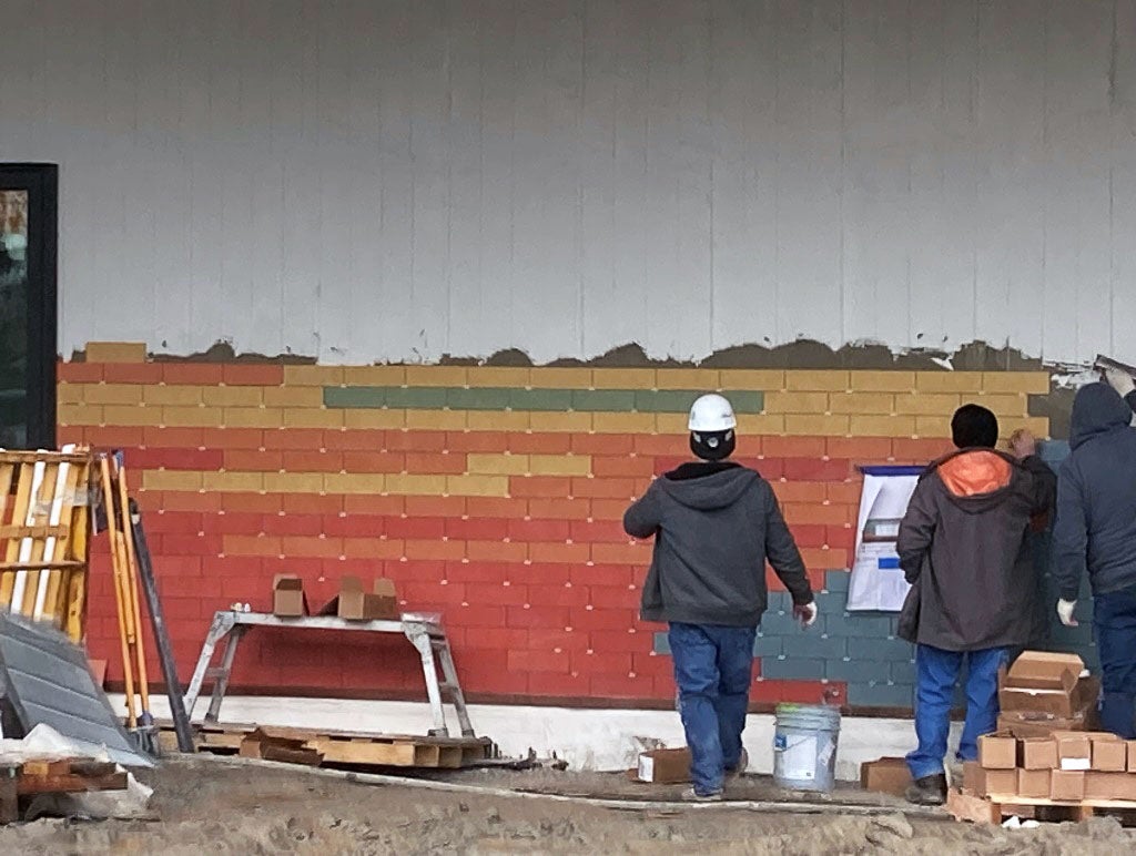 people are looking at brightly colored tiles on a wall. they wall is partly tiled, and partly prepped for tiles