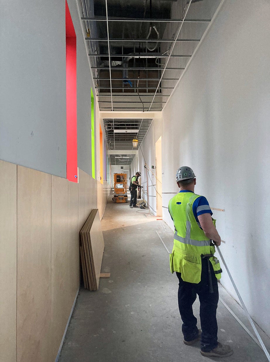 a hallway under construction has people working to install wood panels under windows with colorful window wells