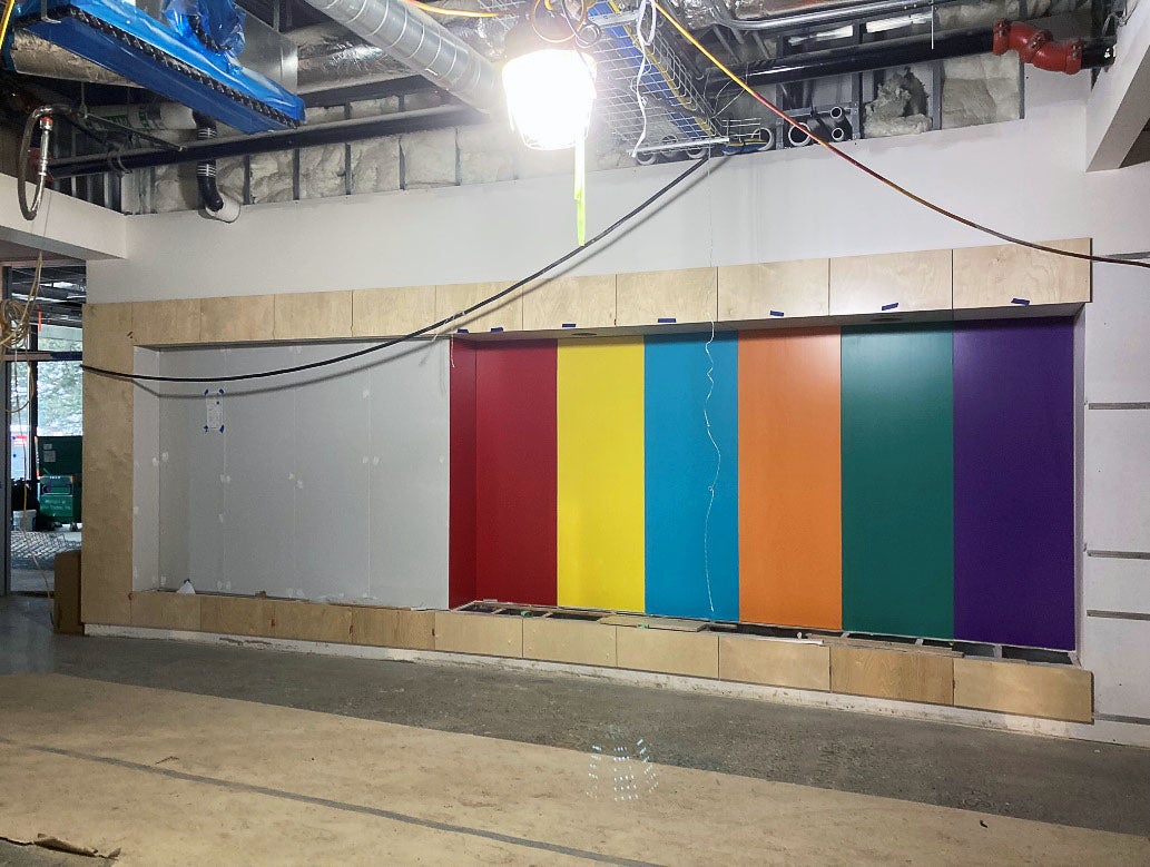 a wall in a room under construction has colorful pieces of wod partially installed with light wood framing around the whole space