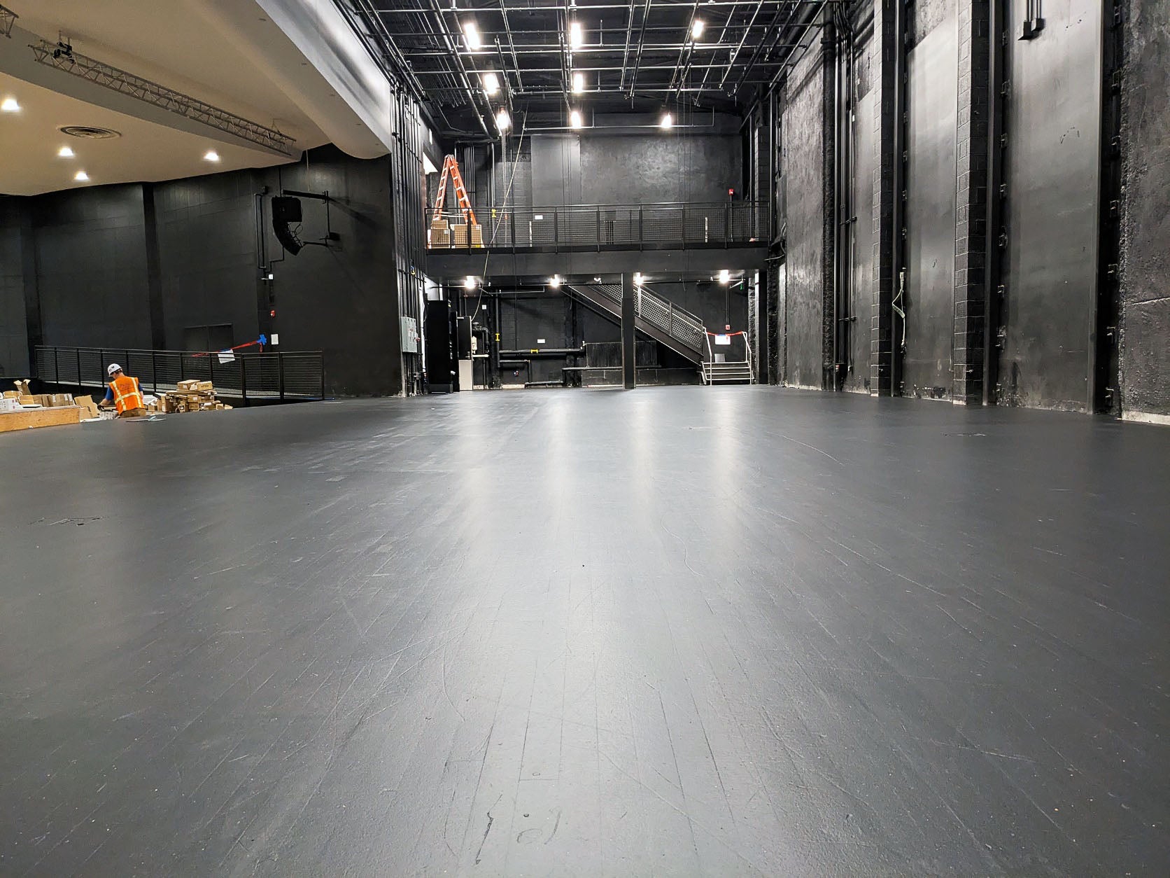 a black floor has black walls and theatre rigging lights above it