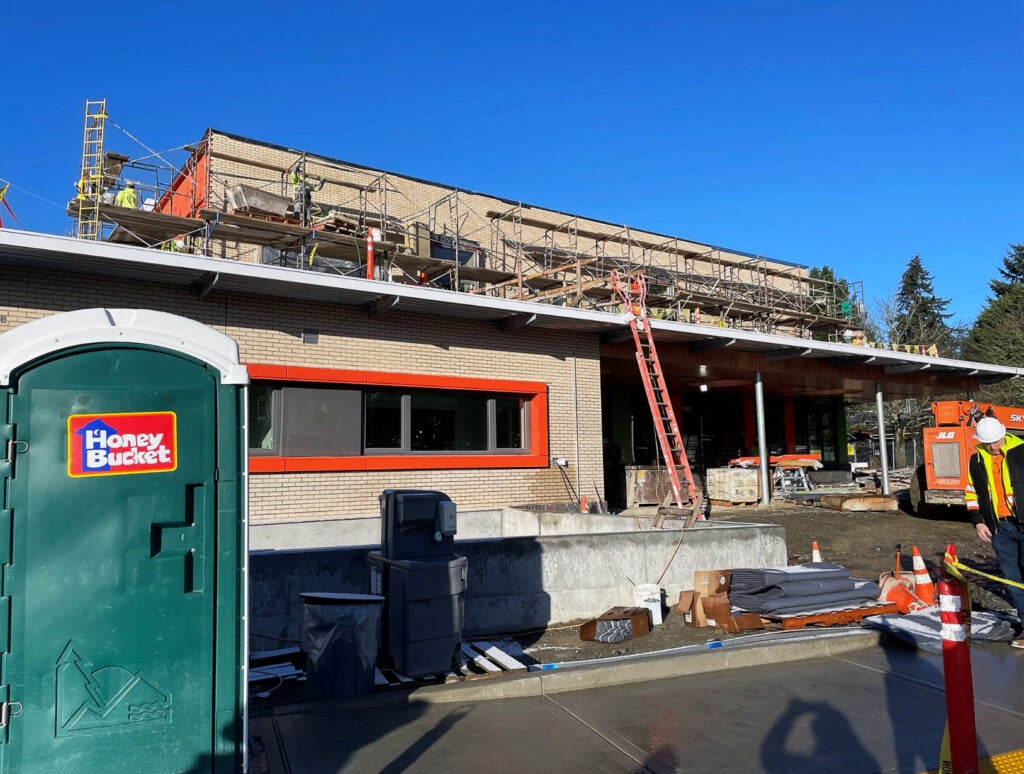 a two story building under construction has a ladder leaning against an overhang over an doorway - bricks are around an orange window