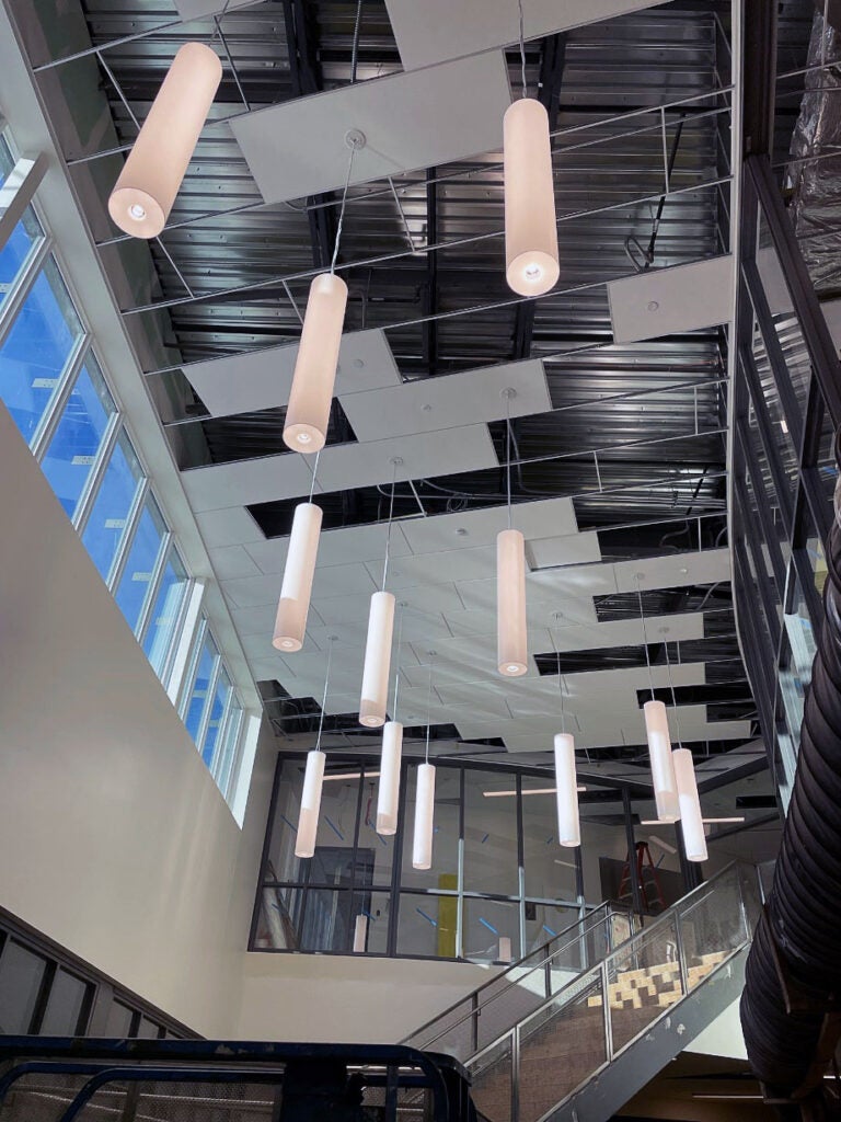 tubular ceiling lights hang from a high ceiling with a stairway below them