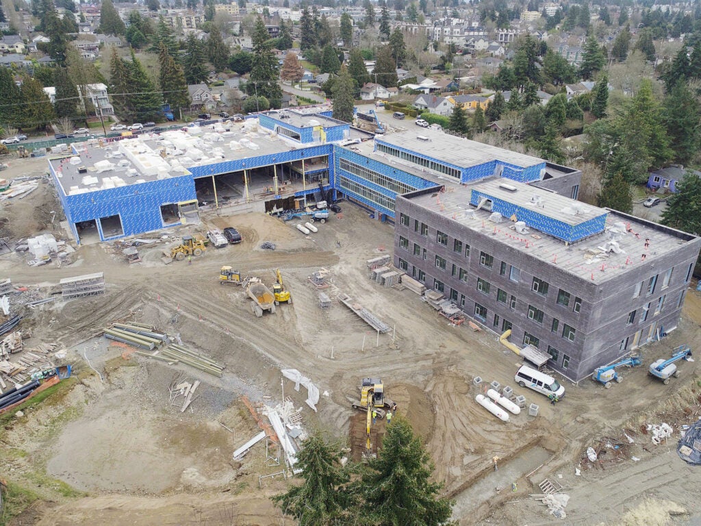 aerial of a large L-shaped building under construction with soil and equipment in between the wings