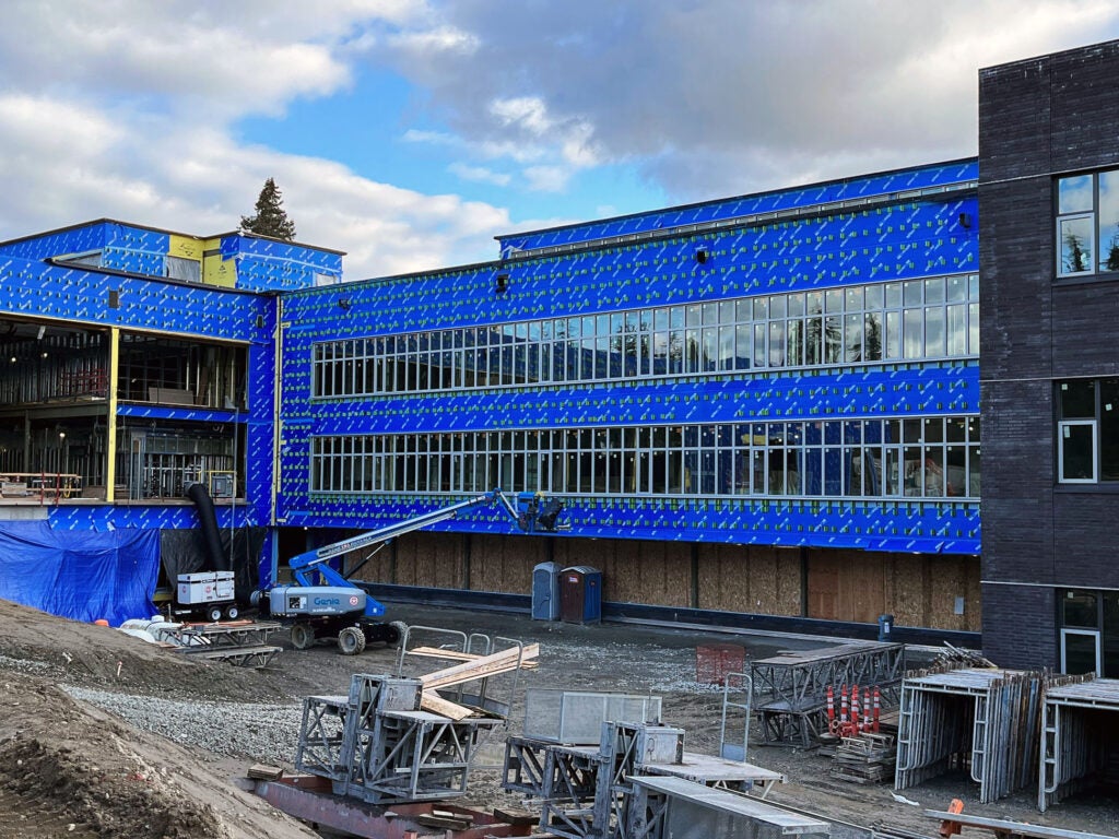 a section of a 3-story building with blue weatherproofing and glass windows