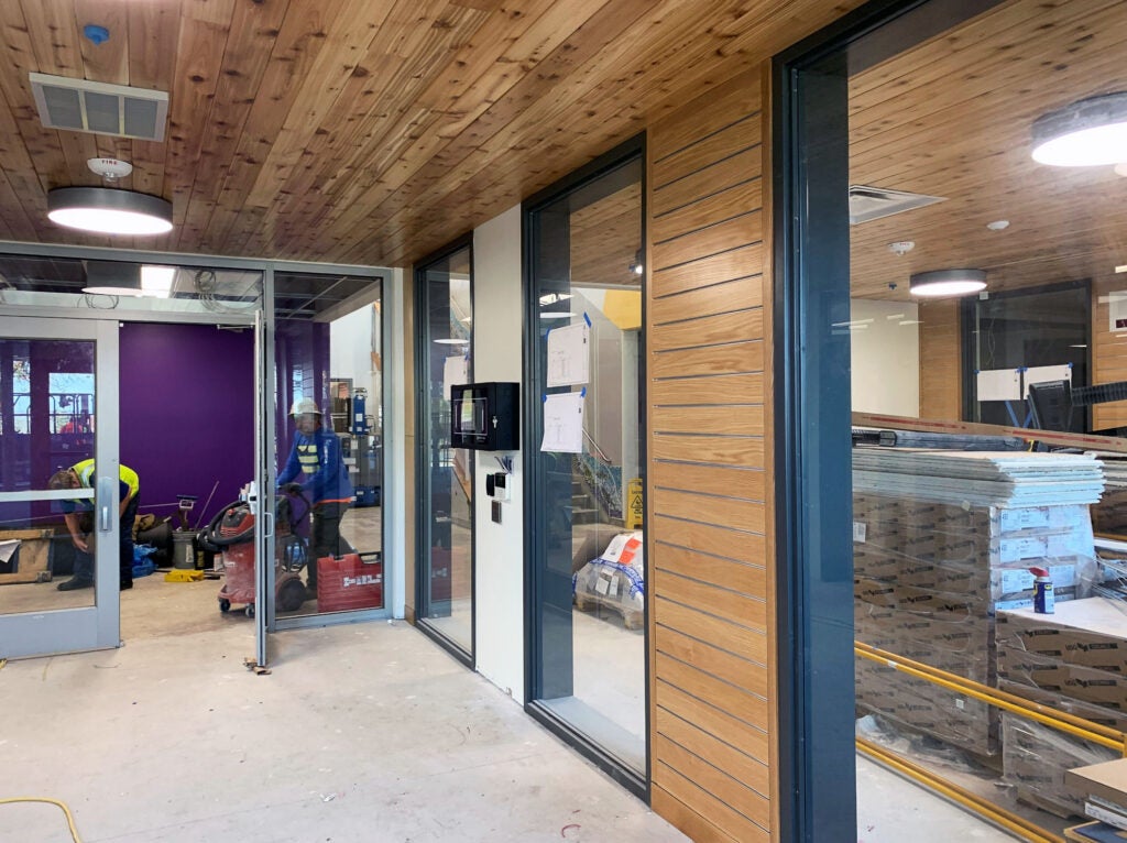 a section of a hallway with wood walls, windows on one side, and a door straight ahead