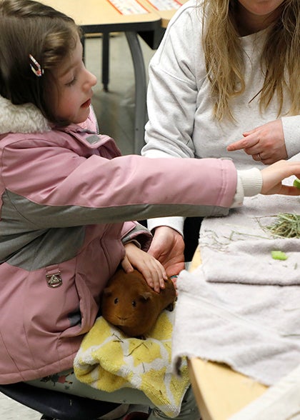 A student holds a guinea pig and talks with a teacher