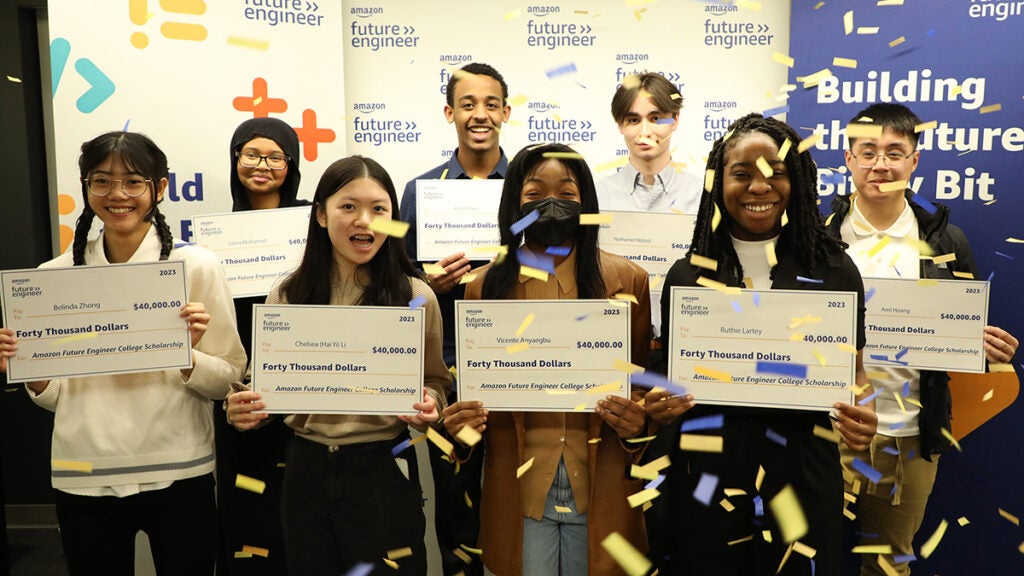 A group of eight students hold large checks while confetti falls on them