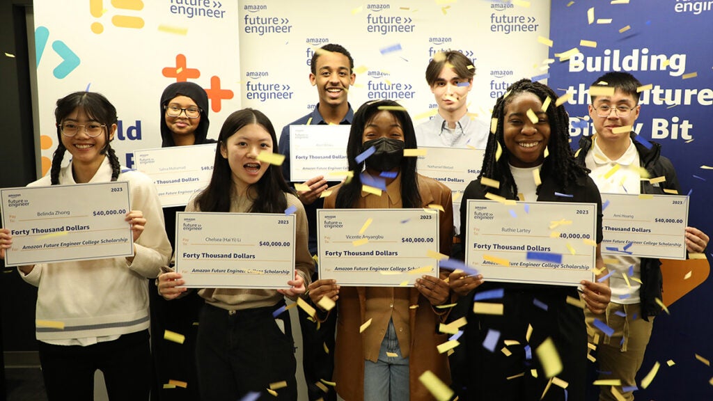 A group of eight students hold large checks while confetti falls on them