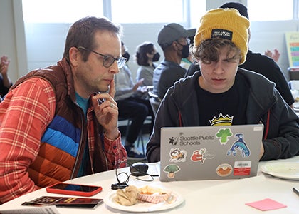 A teacher and student sit together in front of a laptop