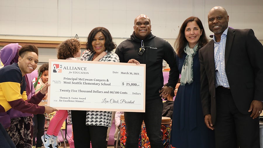 Six people stand together at a school assembly. Principal Conyers holds a giant check for the award.