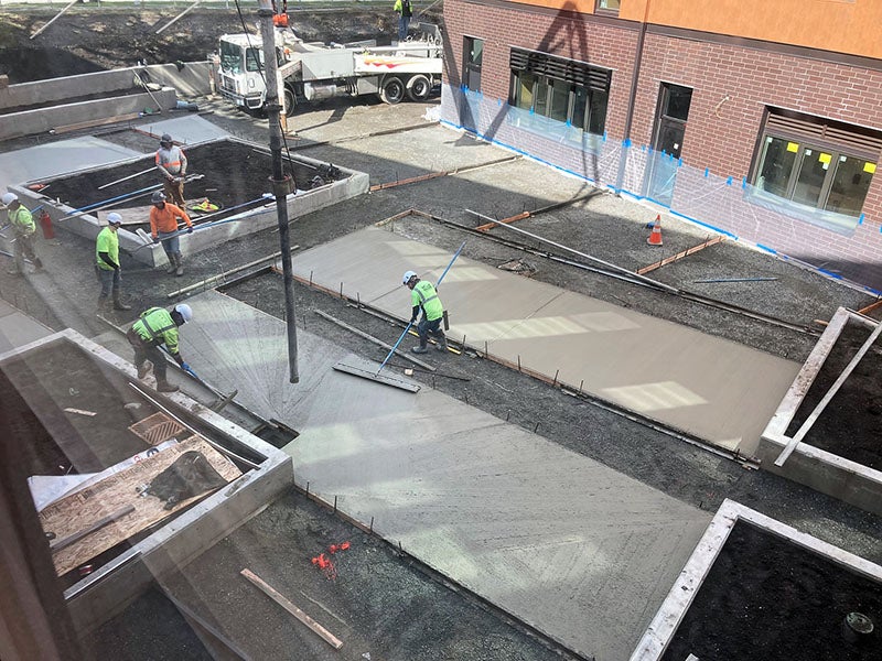 workers are smothing concrete outside of a brick building