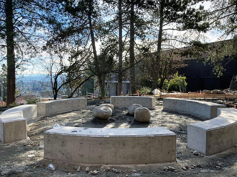 a series of concrete arc shaped benches form a circle with spaces between them to enter. Large rocks are in the middle of the circle