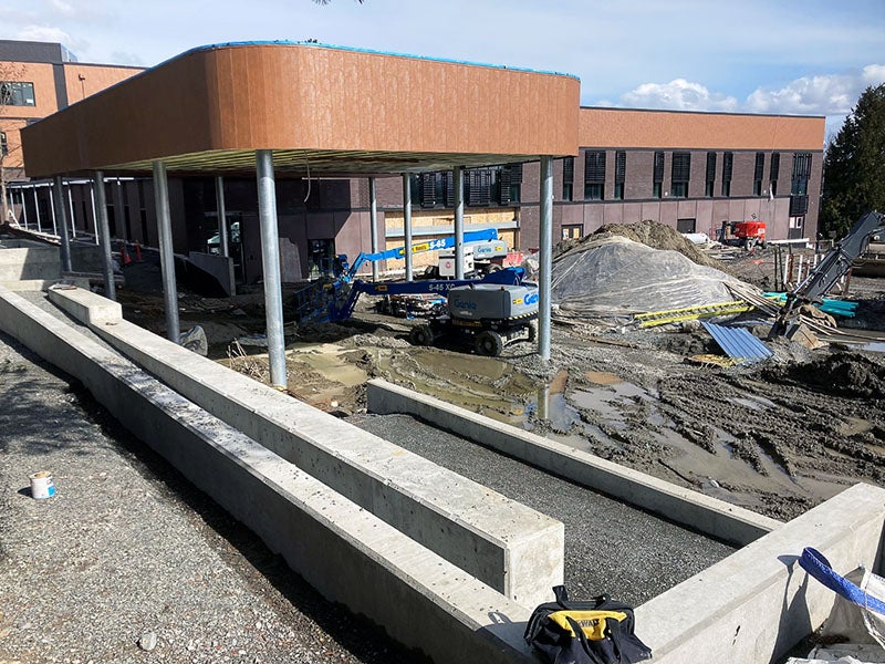 a canopy structure extends from a building next to a concrete wall. Construction equipment is being used under it.