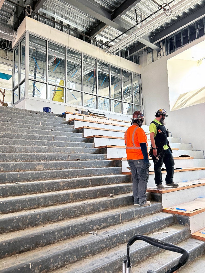 One worker stands on concrete stairs with another on wood stairs that are twice the height