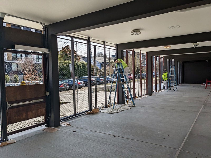 a covered walkway has workers on ladders while painting fence frames