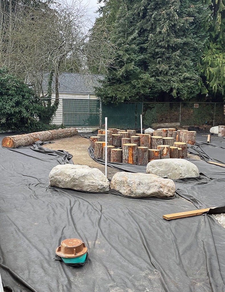 black fabric on the ground with 3 large boulders in a group and a number of logs on end of differing heights