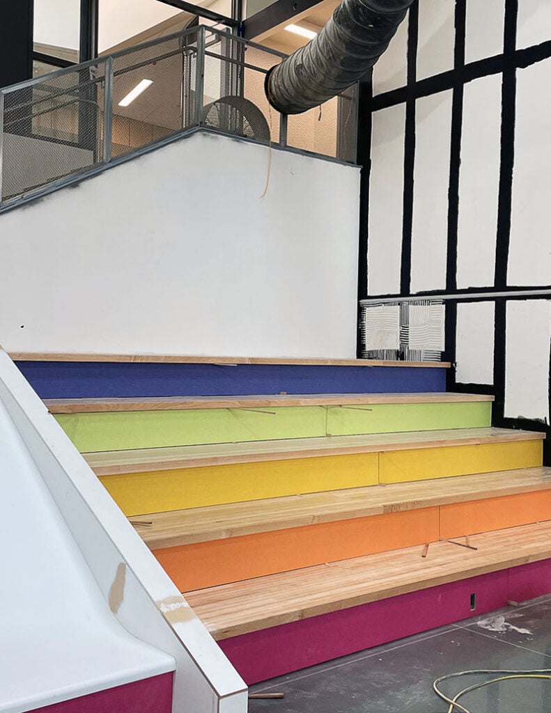 wide and deep stairs have wood tops and colored risers. From top risers are blue, green, yellow, orange, and bright pink