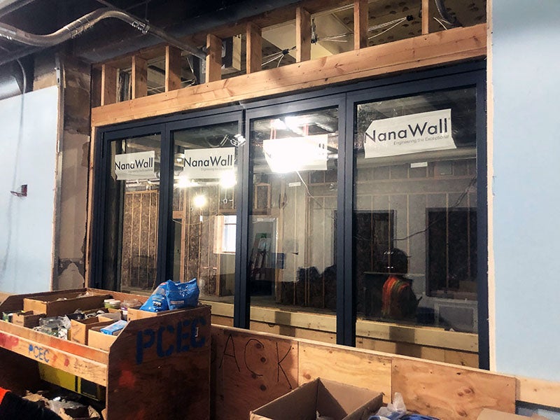 a room underconstruction has four glass panels with black framing between two walls. The glass says "nana wall."