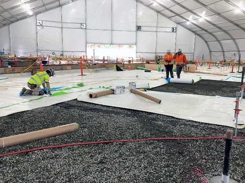 inside a large tent workers are installing white material from rolls over gravel