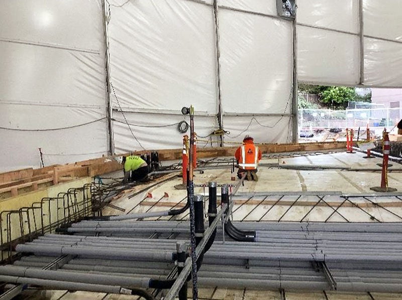 under a large tent, white waterproofing material has a stack of electrical conduit placed in a guie frame with rebar beneath it