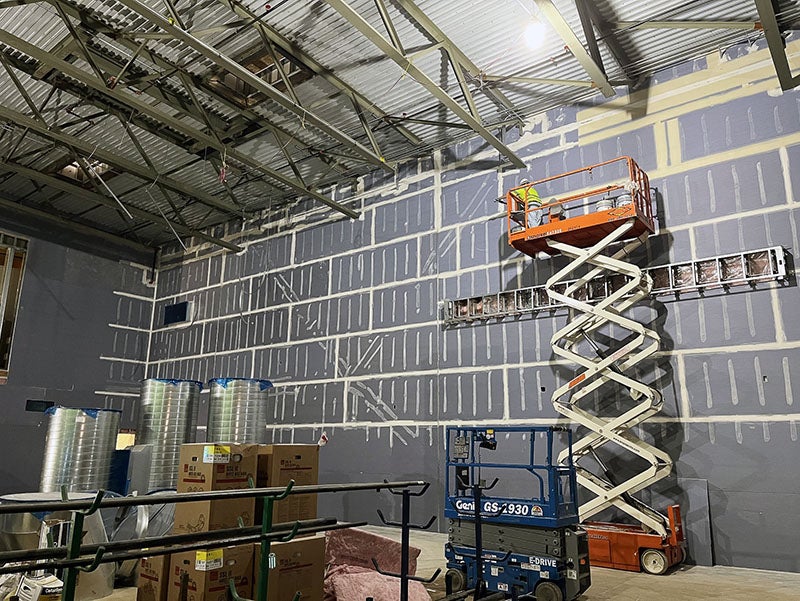 a worker on a scissor lift is taping wallboard in a two story room