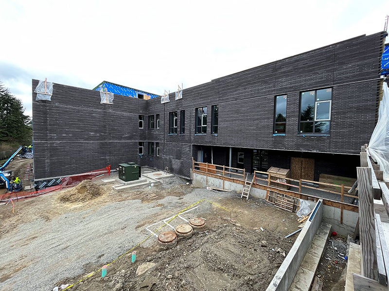 the corner of a dark brick 2 story building with windows forms an L shape with construction materials on the ground