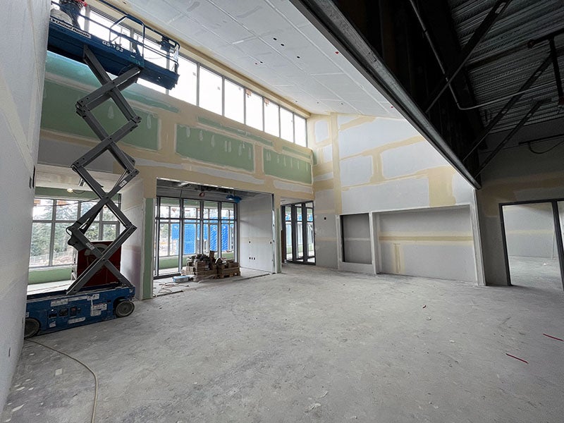 a large volume 2-story room is under construction with taped but not finished wall board, windows and doors, and the bottom part of a scissor lift visible