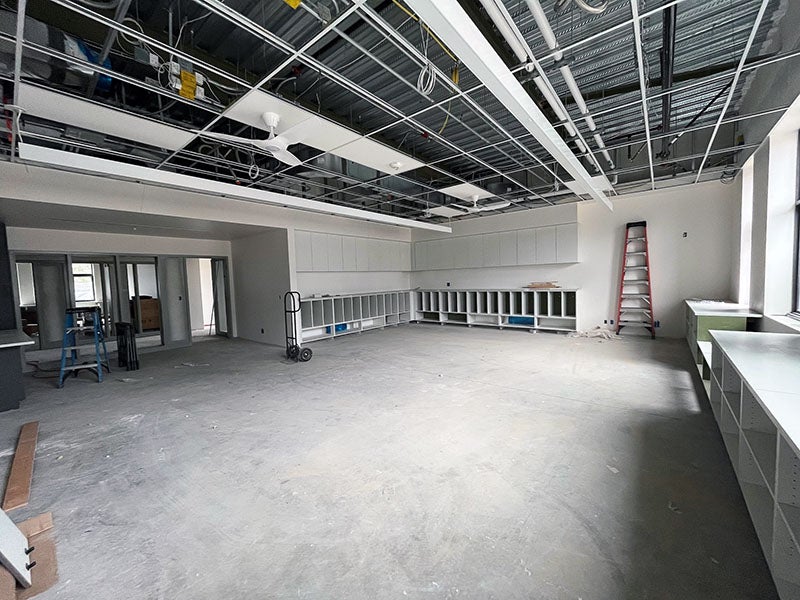 a large room with an open ceiling grid that has a fan and lights installed. casework is around the sides. on the left, doors and windows look out to an interior space