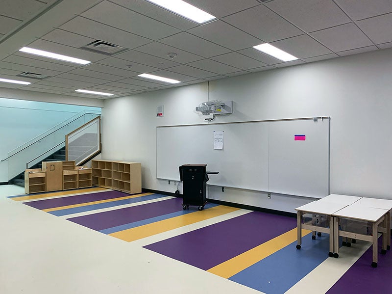 a common area is defined by a striped floor and a learning wall and teacher station