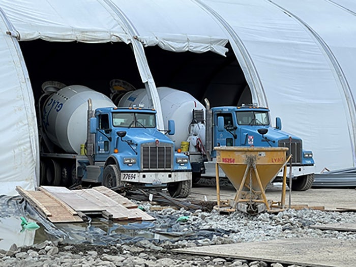 two cement mixer trucks are backed into openings in a large white tent