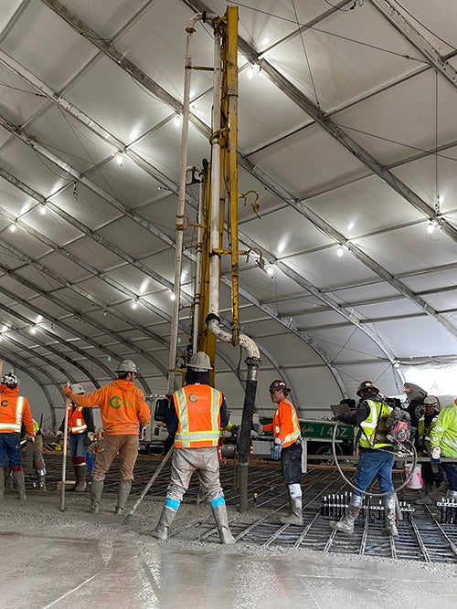 a group of workers in safety vests and hard hats are using a pump from overhead to place concrete in rebar