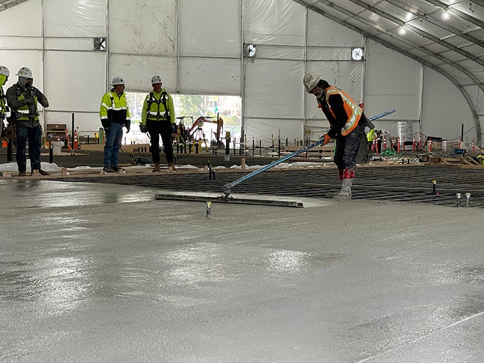 a worker in a safety vest and hardhat is smoothing concrete in a large flat area