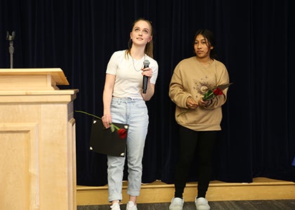 Two students stand at a podium while one of the students addresses the audience