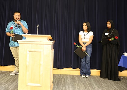 A student stands at a podium talking to the audience while two students listen