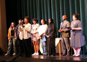 A group of students stands on a school stage during the award ceremony. One student is at a microphone.