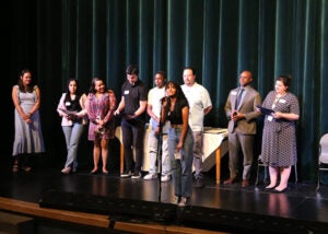 A group of students stands on a school stage during the award ceremony. One student is at a microphone.