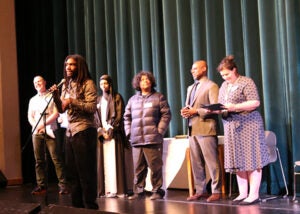 A group of students stands on a school stage during the award ceremony. One student is at a microphone.