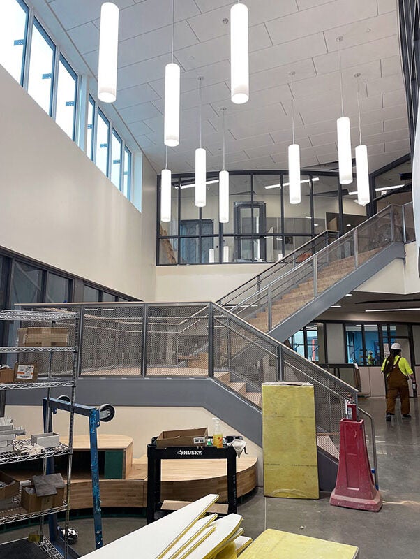 tube shaped light fixtures hang from a high ceiling in a two story space with a stairway