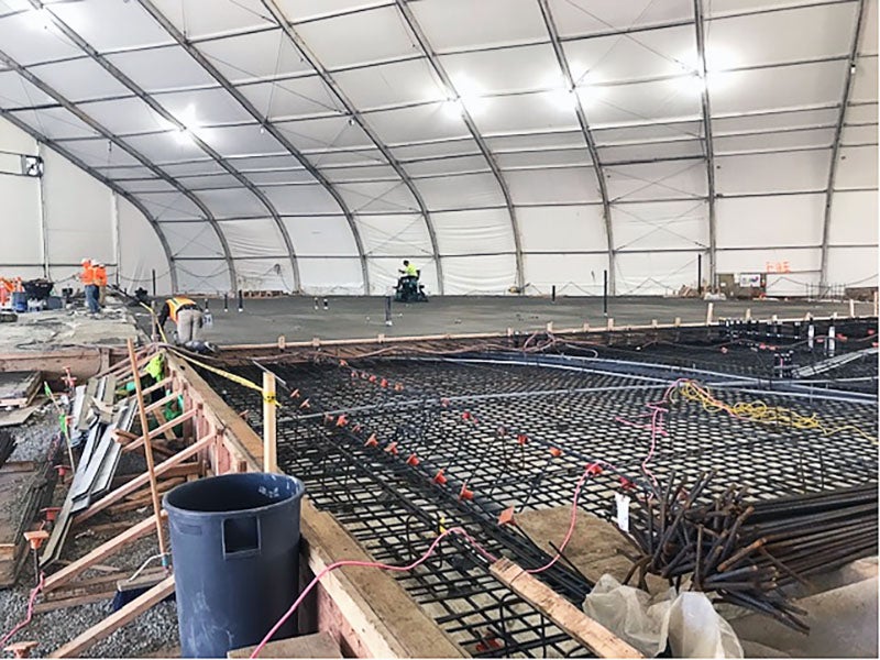 a grid of rebar inside concrete frames under a large tent