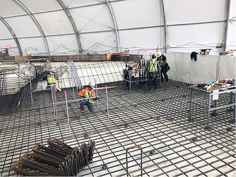 workers installing rebar in a pit under a big tent