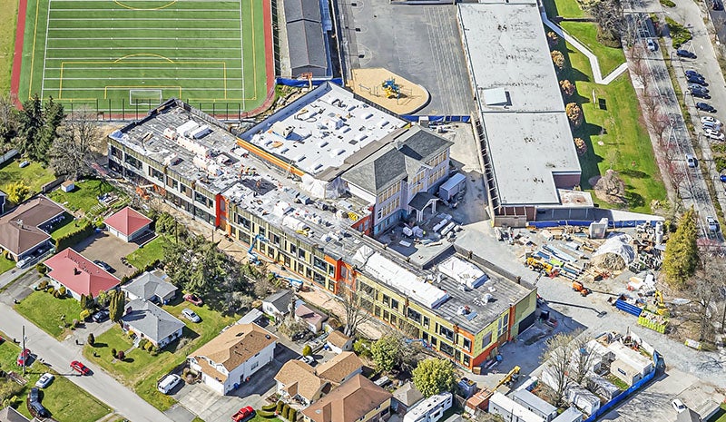 aerial of a buidling under construction with a playfield behind it