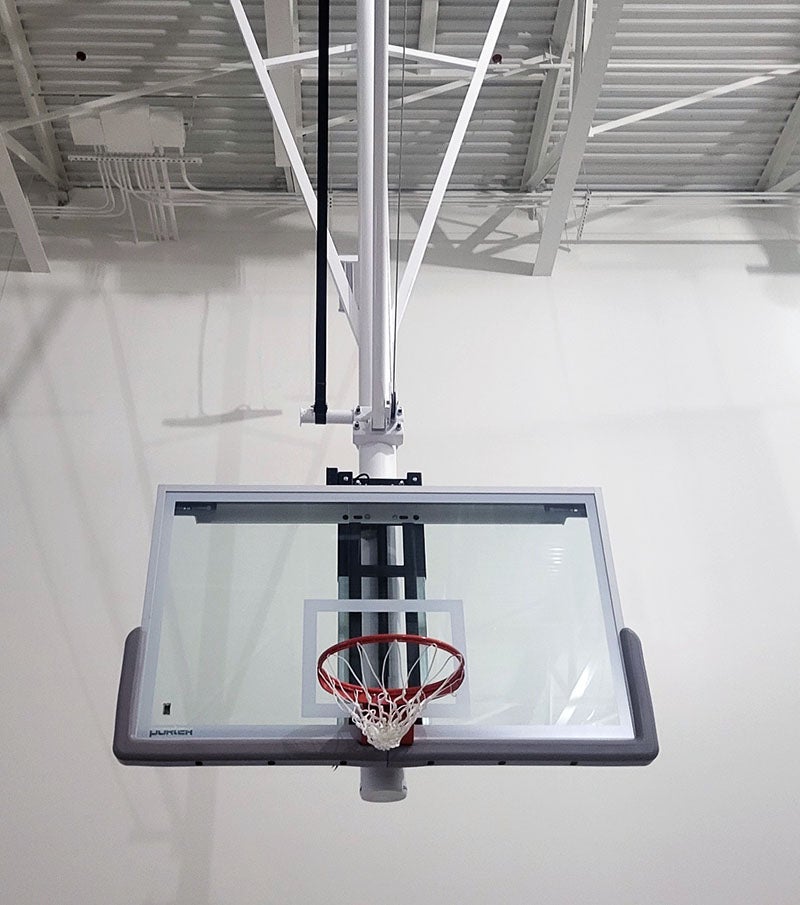 a basketball hoop with clear backboard hangs from ceiling in a large room