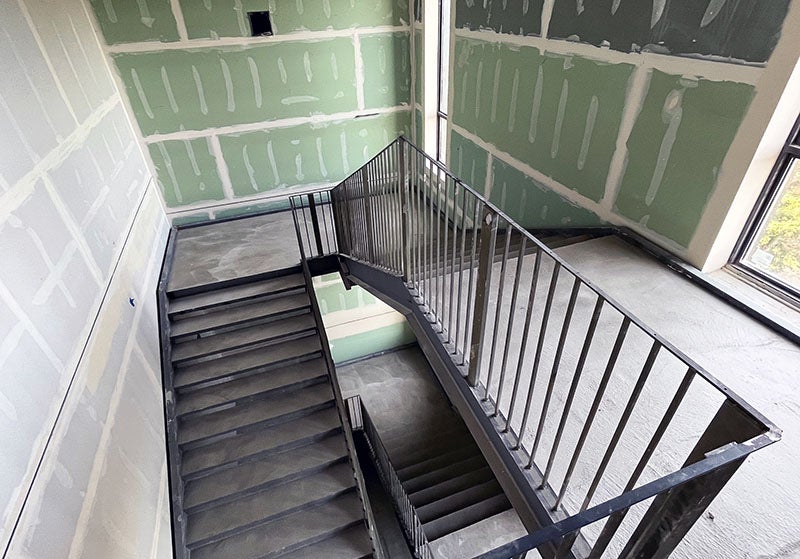 a concrete stairway with green wallboard that has tape and mud on it